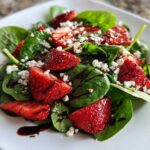 Vibrant close-up of a fresh spinach salad topped with sliced strawberries, feta cheese, and balsamic glaze.
