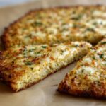 Close-up of two slices cut from a sturdy cauliflower pizza crust topped with melted, browned cheese and parsley.