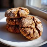 A stack of four rich, brown cinnamon cookies covered in sparkling granulated sugar, sitting on a white plate.