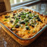 Close-up of hot, cheesy texas trash dip topped with sliced black olives and green onions in a square glass baking dish.