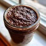 Close-up overhead view of thick, rich chocolate chia pudding texture inside a glass jar.
