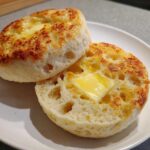 Close-up of two halves of toasted english muffins, showing the signature nooks and crannies filled with melting butter.