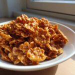 Close-up of crunchy cereal clusters coated in shiny, golden-brown toffee, ready to eat from a white bowl, showcasing the toffee chex mix recipe.