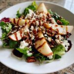 Close-up of a vibrant pear salad featuring sliced pears, crumbled feta, pecans, and a balsamic glaze drizzle.