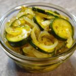 Close-up of sliced zucchini and onions soaking in yellow liquid, resembling bread and butter pickle.