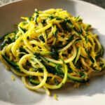 Close-up of bright, spiralized zucchini pasta tossed with herbs and lemon zest.