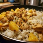 Close-up of juicy chicken pieces and chunks of pineapple mixed with white rice in a skillet, featuring the pineapple chicken and rice dish.