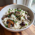 A white bowl filled with fluffy white rice topped with sautéed brown mushrooms and fresh chopped parsley, representing mushroom rice.