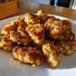 A close-up of crispy, golden brown air fryer lemon chicken bites piled high on a white plate.