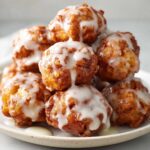A close-up stack of golden brown apple fritter bites drizzled generously with white vanilla glaze.