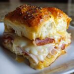 Close-up of a freshly baked club sliders recipe sandwich with melted white cheese and ham on a poppy seed bun.