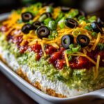 Close-up of a layered hissy fit dip featuring guacamole, salsa, cheese, olives, and green onions.