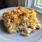 A close-up serving of creamy chicken and rice casserole topped with melted cheddar cheese and crunchy breadcrumbs.