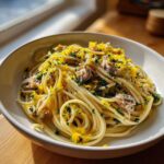 Close-up of a bowl of spaghetti with flaked sardine pasta, bright lemon zest, and fresh parsley.