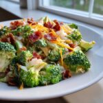 Close-up of a creamy apple broccoli salad topped with crispy bacon bits and shredded cheddar cheese.