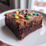 A close-up of a rich, fudgy slice of the best cosmic brownies recipe, topped with chocolate frosting and colorful candy pieces.