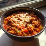A close-up of a bowl of hearty stuffed pepper soup topped with melted white cheese.
