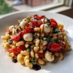 A close-up of a serving of caprese pasta salad featuring small pasta, cherry tomatoes, mozzarella balls, and basil, drizzled with balsamic glaze.