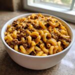 A white bowl filled with creamy cheeseburger pasta featuring elbow macaroni, ground beef, and melted cheddar cheese.