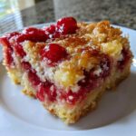 Close-up of a moist slice of cherry pineapple dump cake showing bright red cherries and a golden, crumbly topping.