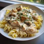 A close-up of chicken mushroom stroganoff served over egg noodles, topped with fresh parsley.