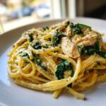 Close-up of a plate of creamy chicken spinach pasta topped with Parmesan cheese and black pepper.