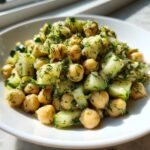 A close-up, bright photo of chickpea cucumber slaw mixed with fresh dill and a light dressing, served in a white bowl.