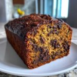 A close-up of a freshly baked, moist chocolate chip banana bread recipe loaf on a white plate.