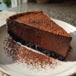A decadent slice of chocolate truffle pie with a dark crust, dusted heavily with cocoa powder.