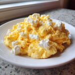 A serving of fluffy, bright yellow cottage cheese scrambled eggs piled high on a white plate.