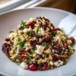 A close-up, appetizing shot of a vibrant cranberry quinoa feta salad mixed with pecans and parsley, served in a white bowl.
