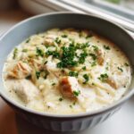 A close-up of creamy chicken orzo soup topped with fresh parsley in a light blue bowl.