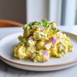 A generous scoop of bright yellow creamy egg salad mixed with chunks of white egg and diced red onion, topped with fresh chives.