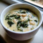 Close-up of a creamy high protein white bean soup featuring white beans and dark green kale in a white bowl.
