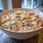 A close-up of creamy, loaded hoagie dip mixed with meat and vegetables in a white bowl.