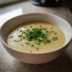 A close-up of a creamy bowl of leek soup topped generously with fresh green chives and black pepper.