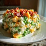 A molded serving of creamy pea salad mixed with cheese cubes and topped generously with crumbled bacon.