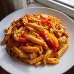 A close-up of a serving of creamy Rasta pasta mixed with chicken pieces and vibrant red and yellow bell peppers.