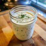 A jar filled with thick, creamy homemade salad dressing topped with fresh chopped chives.