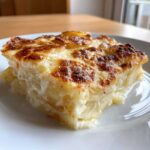 A close-up of a thick, creamy slice of scalloped potatoes recipe with a golden, bubbly, browned cheese top.