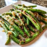 Close-up of perfectly roasted green beans topped with crispy, browned garlic and seasoning.