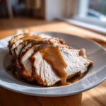 Slices of juicy crockpot turkey breast covered in rich brown gravy, served on a white plate.