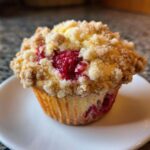 A close-up shot of a single, perfectly baked raspberry muffin topped with a generous layer of golden streusel crumb topping.