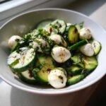A bowl of refreshing cucumber mozzarella salad featuring sliced cucumbers, small mozzarella balls, and fresh basil.