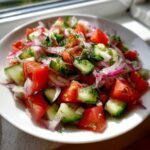 Vibrant close-up of fresh cucumber onion and tomato salad tossed with dill, served in a white bowl.