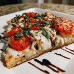 A close-up slice of easy chicken caprese flatbread topped with mozzarella, tomatoes, chicken, and basil.