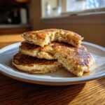 A stack of three fluffy discard pancakes on a white plate, with the top one broken open to show the airy interior.