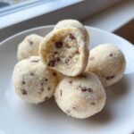 A stack of creamy frozen greek yogurt peanut butter bites with mini chocolate chips, one is cut in half.