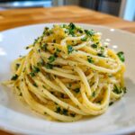 Close-up of a serving of glossy garlic butter pasta tossed with fresh parsley.