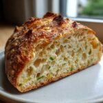 Close-up of a slice of golden-crusted garlic herb dutch oven bread showing an airy crumb with visible herbs.